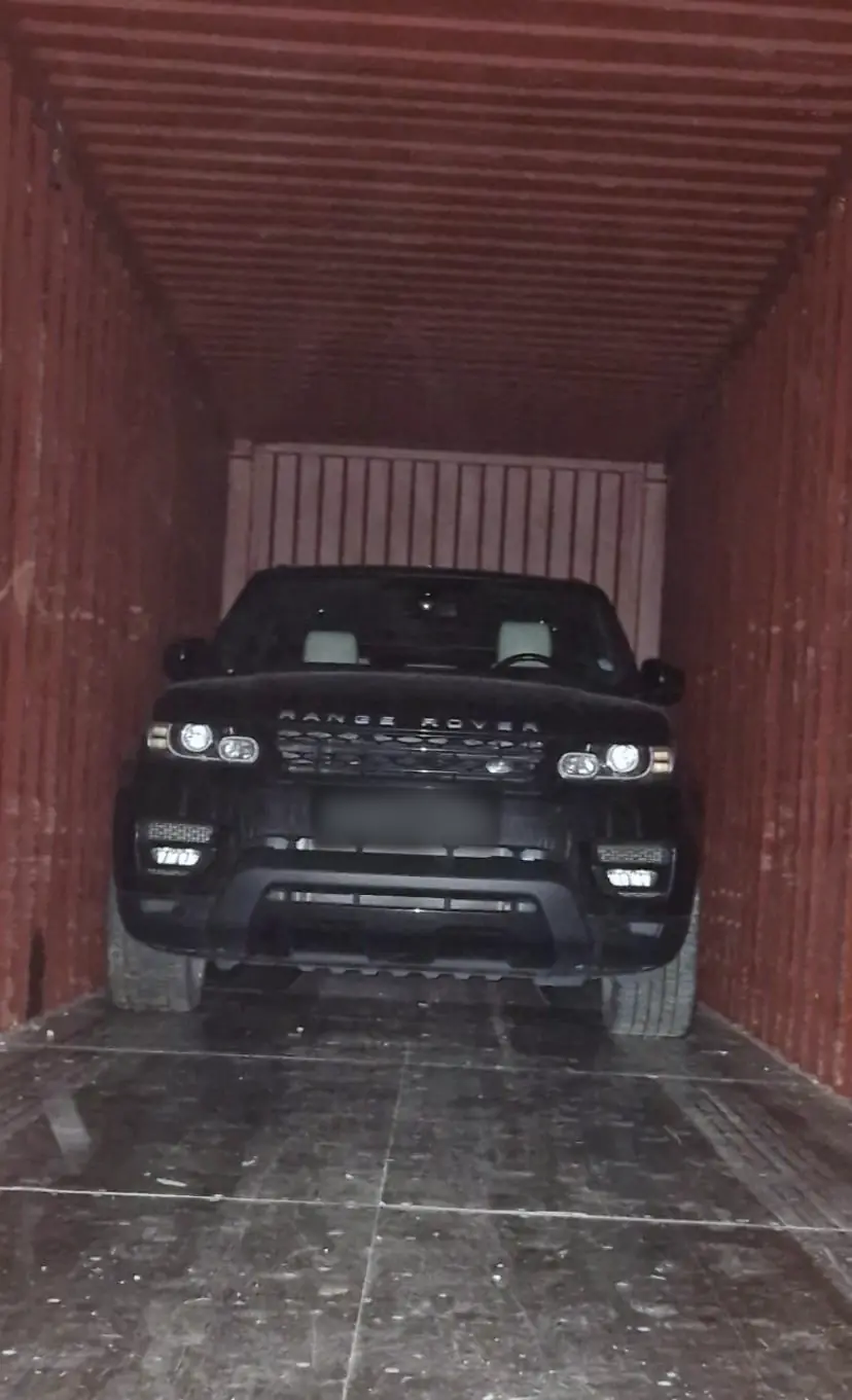 Range Rover Sport kuģu konteinerā ar ieslēgtiem lukturiem